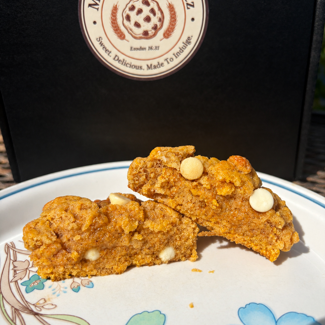 Pumpkin caramel cheesecake cookie broken in half on a floral plate, showing the soft pumpkin interior with white chocolate chips