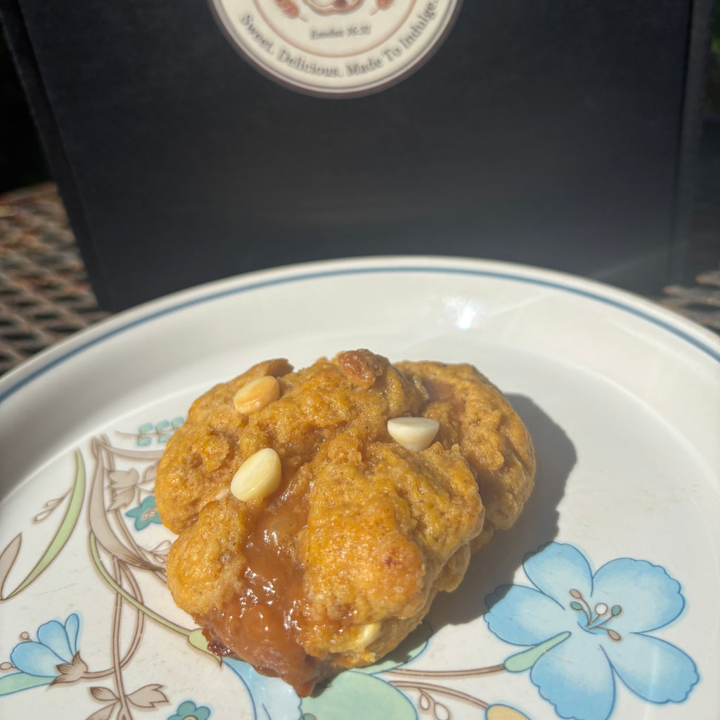 Pumpkin caramel cheesecake cookie with white chocolate chips on a floral plate in front of a Mannazello Treatz bakery box