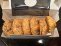 A box of chocolate chip scones, with several golden-brown baked scones visible inside an open white cardboard bakery box on a dark countertop.