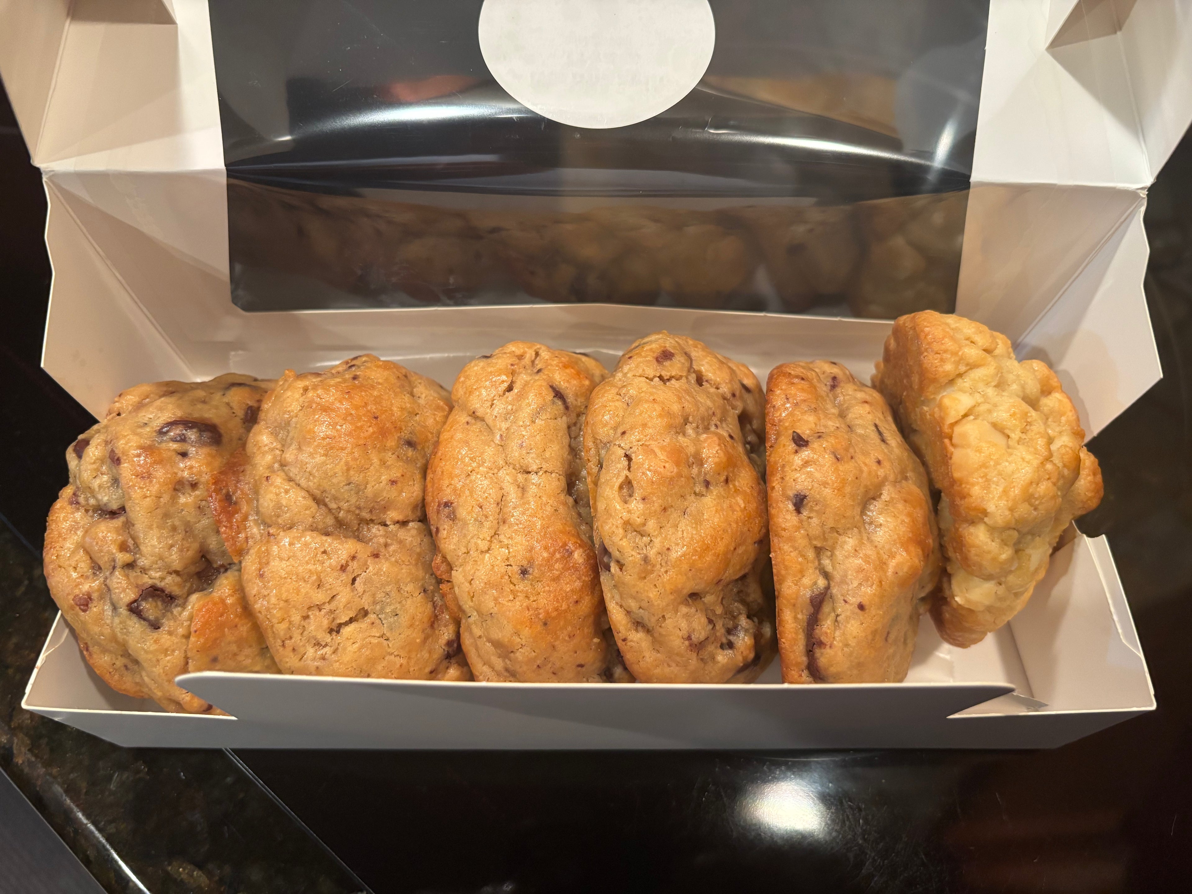 A box of chocolate chip scones, with several golden-brown baked scones visible inside an open white cardboard bakery box on a dark countertop.