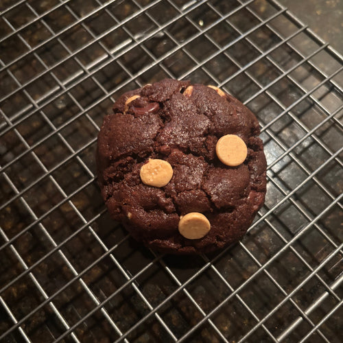 Dark chocolate Brown Butter Double Chocolate Peanut Butter Cookie topped with peanut butter chips, on a wire cooling rack