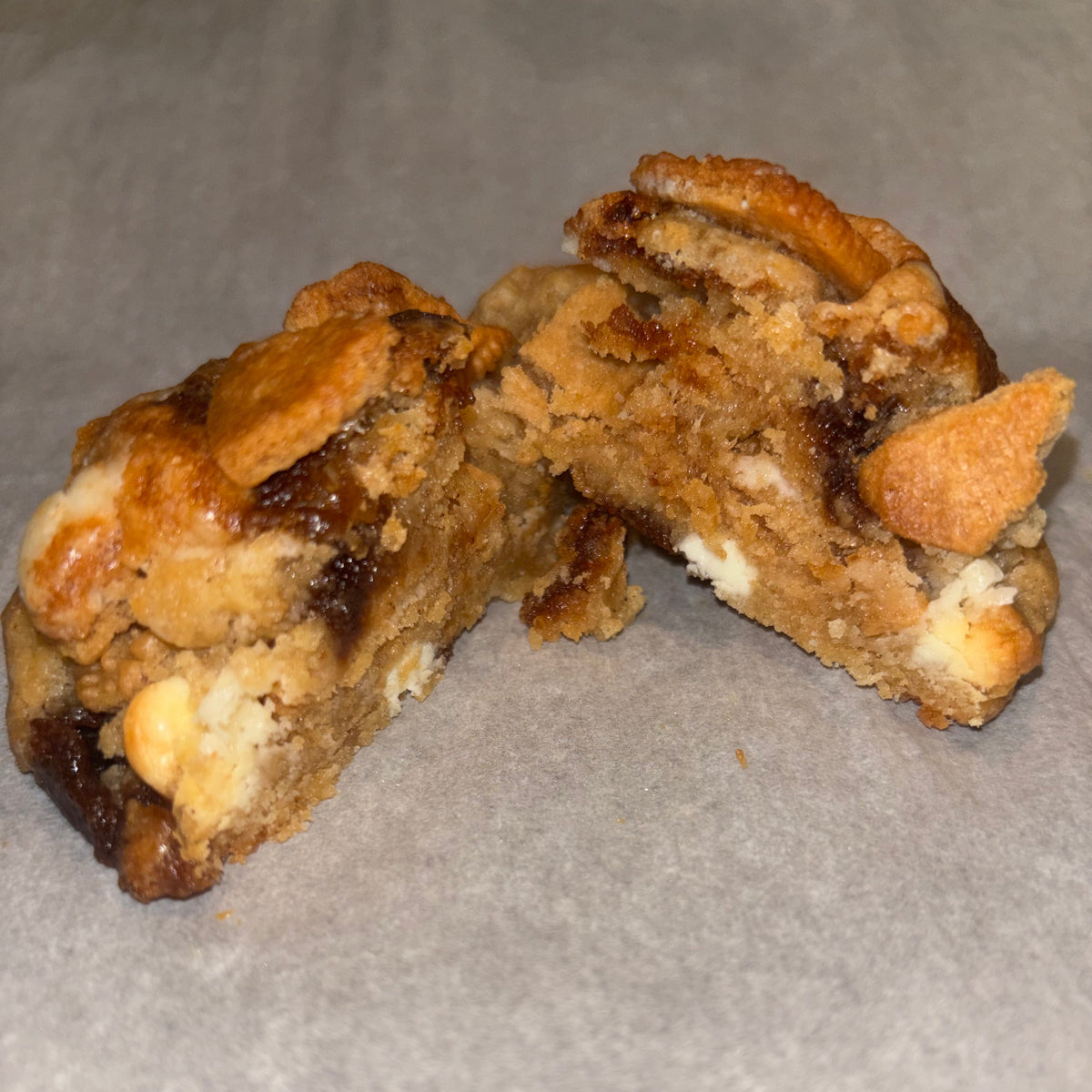 Cinnamon Roll Cookie broken in half, showing a gooey cinnamon-swirled interior with cinnamon roll Oreo pieces and cream cheese chips
